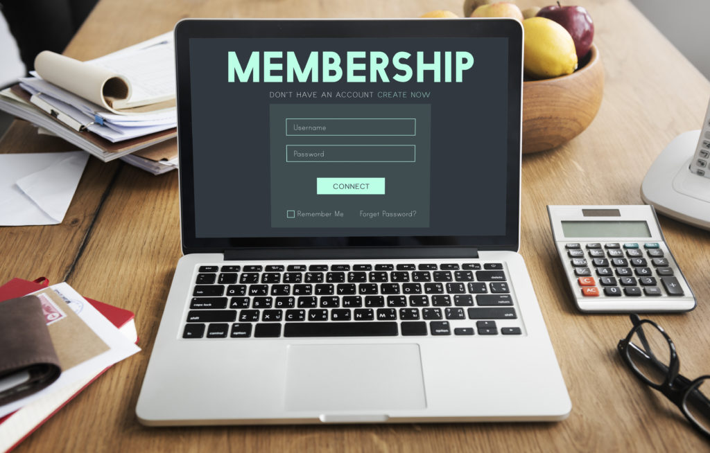 Laptop showing membership log in screen on table with other work related items including calculator, glasses and paperwork.